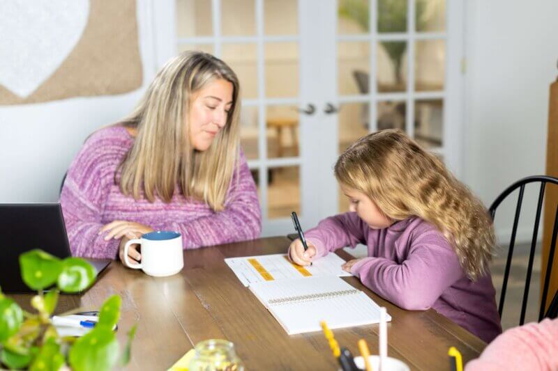 girl writing while mom helps