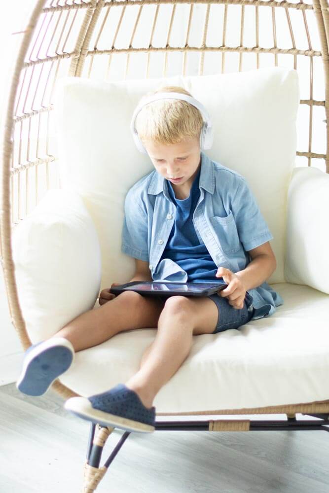 Boy sits on chair while watching an educational video on his tablet