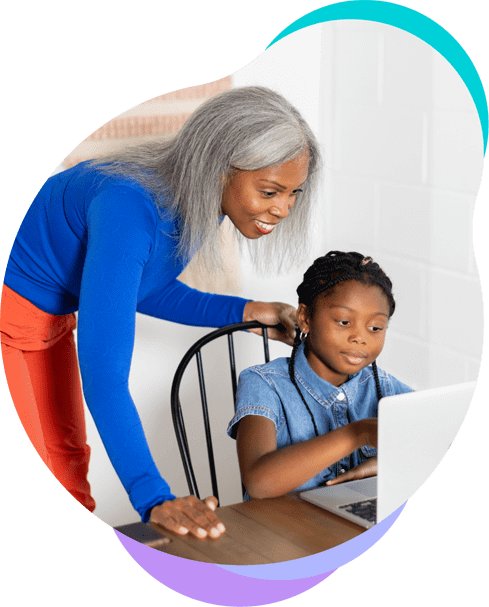 Mother stands behind her daughter as she completes an assignment on her laptop.