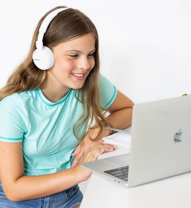 Girl wearing headphone smiles at her laptop while she is being tutored virtually